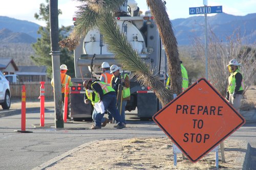 Prepare to Stop Sign Displayed as Construction Workers Work in the Background