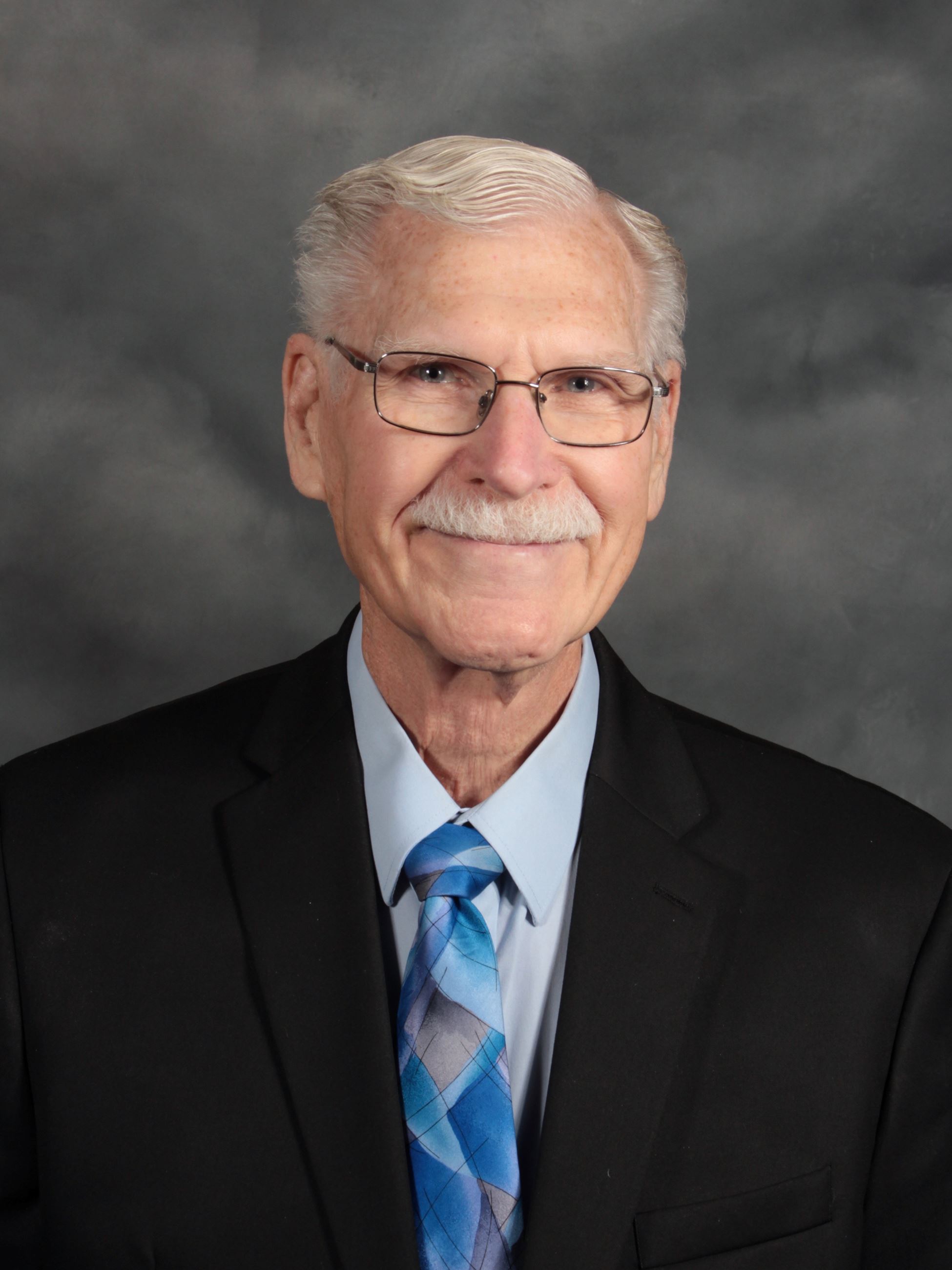 Man with glasses in a black suit with blue tie (jpg)